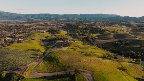 Drone-Slowly-Flying-Over-Gentle-Rolling-Hills-in-Wine-Country-of-Santa-Ynez-California,-Vineyards-Below-and-Mountain-Range-on-Horizon