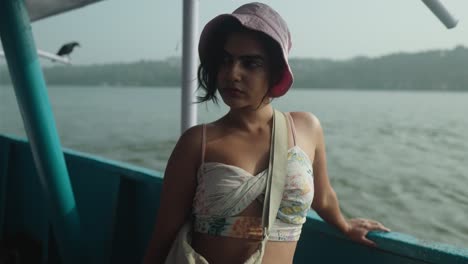 Young-woman-in-a-white-bikini-is-standing-on-a-boat-with-a-pink-hat-on-in-India