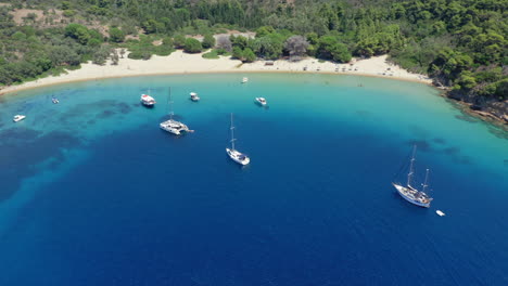 Aerial:-Panoramic-drone-shot-of-Tsougria-island-beach-near-Skiathos,-Sporades,-Greece-with-moored-sailboats-and-catamarans