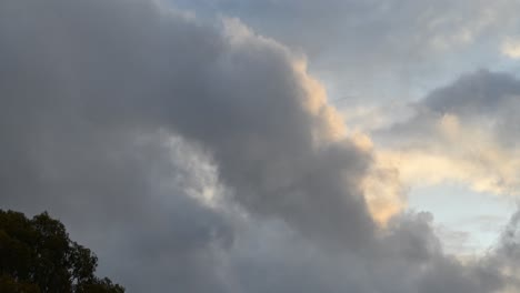 Ein-Zeitraffer-Der-Wolken,-Die-An-Einem-Stürmischen,-Launischen-Tag-Durch-Den-Himmel-Ziehen,-Mit-Einem-Baum,-Der-Sich-Im-Wind-Bewegt
