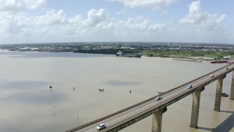 Wide-angle-aerial-shot-of-Jules-Wijdenbosch-Bridge-between-Paramaribo-and-Meerzorg-in-Suriname,-South-America,-with-heavy-traffic-as-drone-gains-backwards,-revealing-bridge