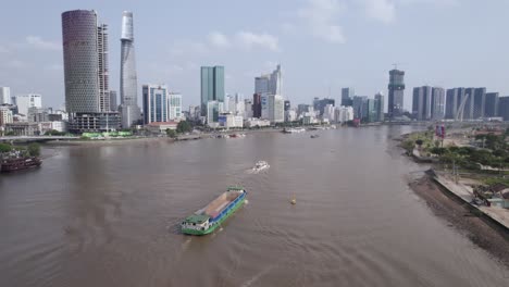 Blick-Auf-Einen-Fluss-Mit-Einem-Logistischen-Frachttransport-Containerschiff-Und-Der-Modernen-Ho-Chi-Minh-Stadt-In-Vietnam-Im-Hintergrund
