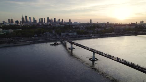 Menschen,-Die-In-Der-Abenddämmerung-In-Warschau,-Polen,-über-Die-Agrafka-Brücke-über-Die-Weichsel-Mit-Blick-Auf-Die-Stadt-Spazieren