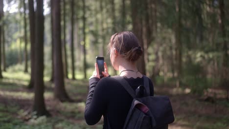 Young-girl-with-a-backpack-captures-the-beauty-of-the-forest-on-her-phone