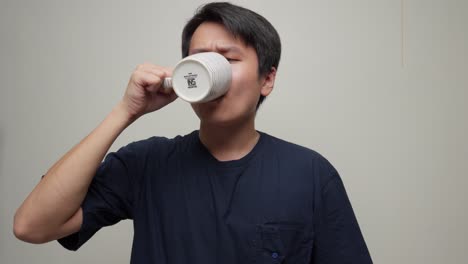 Closeup-portrait-shot-southeast-asian-young-man-drinks-white-cup-inside-room-face-expression-swallowing-liquid