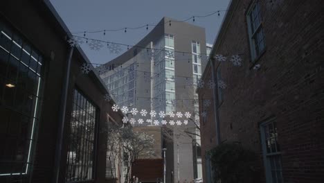 This-is-a-wide-shot-of-a-dimly-lit-alleyway-in-Nashville,-adorned-with-festive-snowflake-lights,-contrasted-by-the-modern-building-at-the-end,-under-an-evening-sky