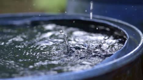 Rain-drops-filling-up-rainwater-harvesting-barrel,-closeup-slow-motion