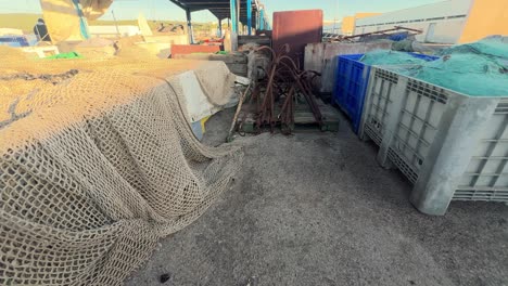 Sauntering-among-the-fishing-gear-housed-in-the-fishing-village's-warehouse,-observing-aged-metal-anchors-and-crates-brimming-with-fishing-nets