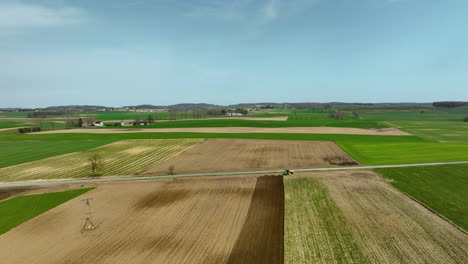 Flying-Above-Arable-Farmland-With-Farming-Tractor-At-Work-On-Sunny-Day