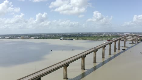 Toma-Aérea-De-Gran-Angular-Del-Puente-Jules-Wijdenbosch-Entre-Paramaribo-Y-Meerzorg-En-Surinam,-Sudamérica,-Con-Tráfico-Mientras-Drones-Vuela-Y-Orbita-Sobre-El-Puente.