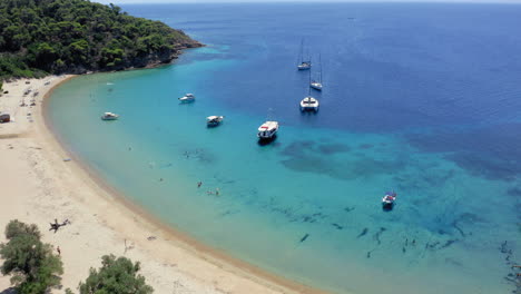 Aerial:-Panoramic-view-of-Tsougkria-island-beach-with-many-tourist-boats-and-sailboats