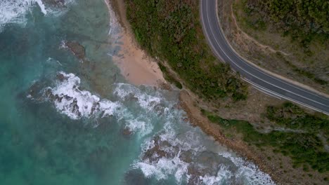 Bird's-eye-drone-view-of-Great-Ocean-Road-curved-highway-turn-with-white-car-and-surf-waves,-Victoria,-Australia