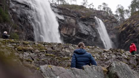 Chica-Adolescente-Mirando-La-Cascada-De-Noruega,-Revelación-Cinematográfica-Desde-Detrás-De-Una-Roca