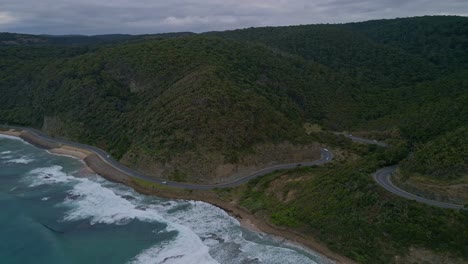 Tilt-Drohnen-Luftaufnahme-Der-Berühmten-Küstenautobahn-Great-Ocean-Road-Mit-Autoverkehr-Und-Waldbergen,-Victoria,-Australien