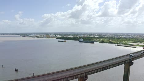 Close-aerial-shot-of-Jules-Wijdenbosch-Bridge-between-Paramaribo-and-Meerzorg-in-Suriname,-South-America,-with-traffic-as-drone-orbits-oil-tanker-ship