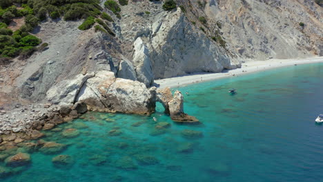 Aerial:-Flying-over-the-limestone-arch-rock-formation-in-Lalaria-beach-in-Skiathos-island,-Sporades,-Greece-with-turquoise-and-emerald-crystal-clear-water
