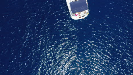 Aerial:-Top-down-reveal-drone-shot-of-a-moored-sailboat-in-blue-sea