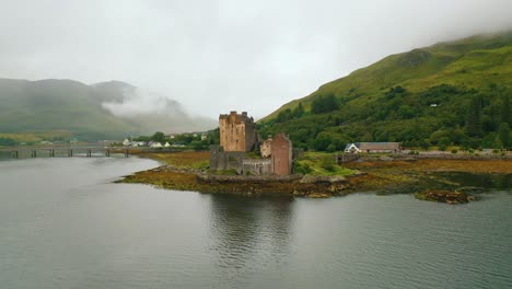 Wide-Aerial-Pan-of-Historic-Eilean-Donan-Castle-on-Loch-Duich,-Scottish-Highlands-in-Autumn-on-Cloudy-day,-Scotland,-United-Kingdom