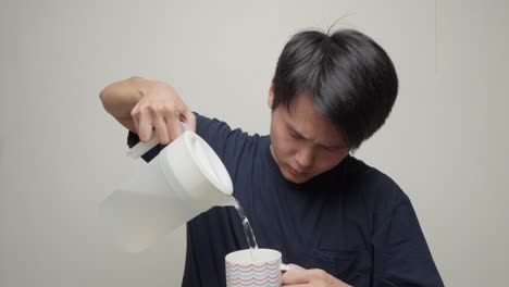 Young-man-pours-refreshing-water-from-transparent-beaker,-drinks-from-mug