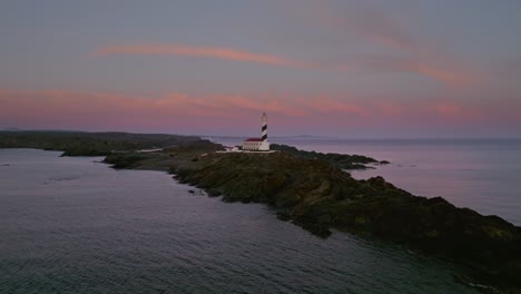 Aerial-drone-fly-above-Menorca-peninsular-lighthouse-landscape-at-sunset-pink-skyline-golden-hour,-Spanish-landmark