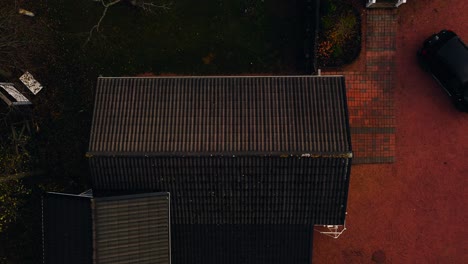 Top-down-drone-shot-above-a-mossy-on-a-garage-roof,-fall-day-at-a-countryside-house