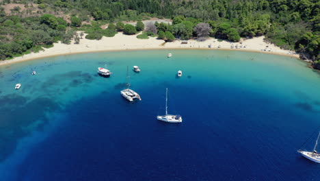 Aerial:-Panoramic-shot-of-Tsougria-island-beach-near-Skiathos,-Sporades,-Greece-with-moored-sailboats-and-catamarans