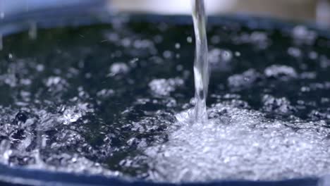 Rainwater-filling-up-harvesting-barrel,-closeup-slow-motion-pouring-creating-bubbles,-slow-zoom