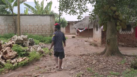 Un-Joven-Tanzanio-Caminando-Por-Calles-De-Tierra-En-Una-Aldea-Rural-Pobre-Usando-Flores-De-Achiote-En-El-Cabello