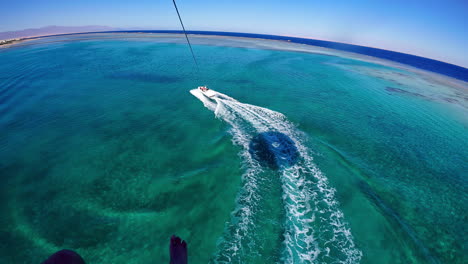 The-downward-view-of-a-tourist-parasailing-behind-a-speedboat-over-an-azure-ocean