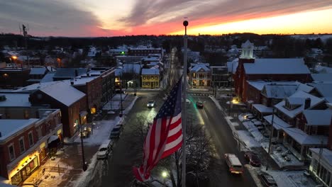 American-flag-waving-over-snowy-town-square-in-USA-during-winter-sunset