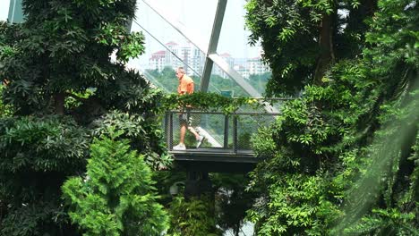 Tourist-walking-across-the-aerial-walkway-at-the-cloud-forest-greenhouse-conservatory,-visiting-the-touristic-Gardens-by-the-bay-in-Singapore