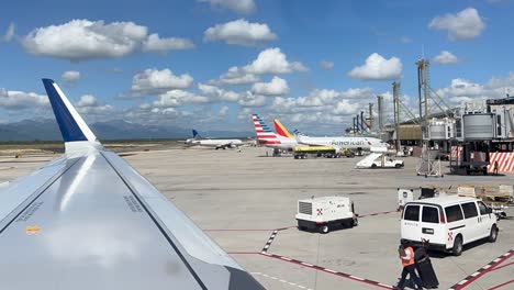 Ventana-De-Avión-En-El-Ala-Con-El-Personal-De-Tierra-Del-Aeropuerto-Moviendo-Unidades-De-Energía-Terrestres