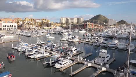 Cabo-marina-of-boats-on-a-cloudy-day,-rising-aerial-view-over-resorts,-Baja-Mexico