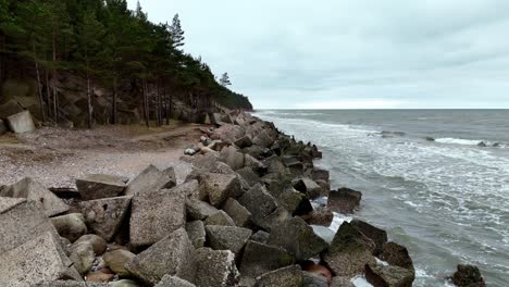 Vista-Lateral-De-Los-Rompeolas-Que-Protegen-La-Playa-Con-Un-Frondoso-Bosque-A-La-Izquierda-En-Kurzeme,-Letonia