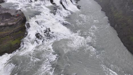Gullfoss,-Iceland,-Flying-Above-Waterfall-and-River-Cascades-With-Tourist-on-Viewpoint,-Drone-Shot-60fps
