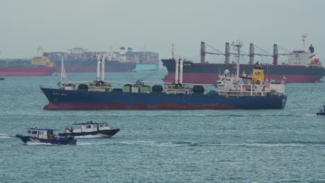 Grandes-Buques-De-Carga-En-El-Estrecho-De-Singapur,-Barcos-De-La-Autoridad-Gubernamental-Navegando,-Inspeccionando-Las-Mercancías-Aduaneras-Y-Documentándolas-Antes-De-Que-Lleguen-Al-Interior.