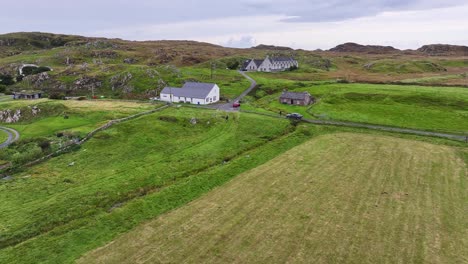 Iona,-Scotland-UK,-Aerial-View-of-Car-Moving-on-Village-Road-Between-House-and-Green-Grassland,-Drone-Shot