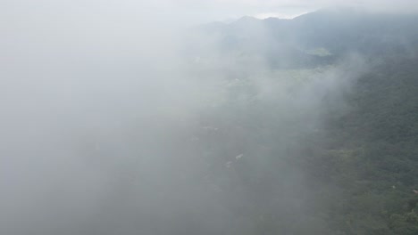 Drone-shot-through-the-clouds-high-over-a-single-mountain-road-of-the-Sierra-Nevada-forest,-Colombia