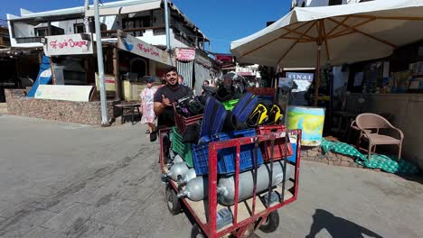 El-Hombre-Egipcio-Local-Lleva-Equipo-De-Buceo-En-La-Playa-De-Dahab,-Lugar-Turístico-De-Egipto-A-Lo-Largo-De-Clientes-Caucásicos