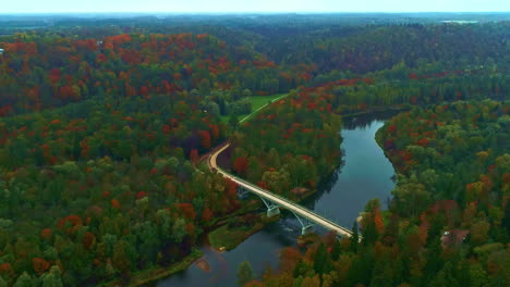 Autumnal-green-orange-yellow-trees-landscape-wide-greenery-with-river-between-flowing,-pristine-natural-environment-aerial-drone-panoramic-slow-motion-fly-view