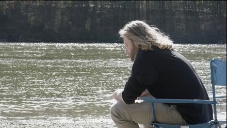 a-young-man-with-long-blond-hair-sits-thoughtfully-in-his-camping-chair