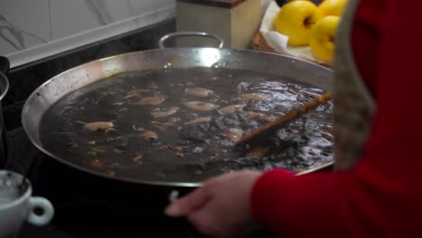 Chef-cooking-squid-ink-paella,-stirs-steamy-black-water-and-shakes-frying-pan