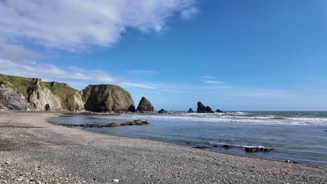 deserted-beach-shingle-sea-cliffs-and-sea-stacks-gentle-waves-in-blue-lagoon-on-a-spring-day-in-Waterford-Ireland