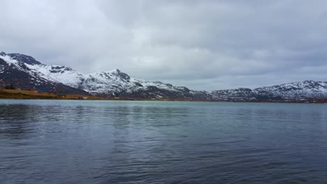 Panoramic-view-of-lake-surrounded-by-snowy-mountains-in-a-cloudy-day