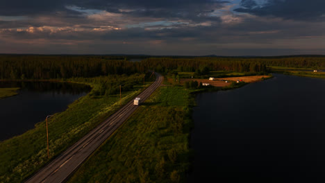 Aerial-view-circling-a-RV-driving-on-road-E75,-summer-evening-in-Sodankyla,-Finland