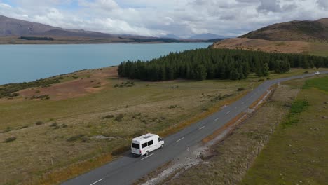 Vista-Aérea-De-Una-Caravana-Conduciendo-Por-Una-Carretera-Junto-Al-Lago-Tekapo.