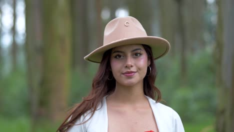 Schönheit-Einer-Ecuadorianischen-Frau-Mit-Hut-Und-Weißem-Oberteil-Und-Offenem-Haar,-Die-Im-Wald-Ruhe-Findet,-Die-Augen-Schließt-Und-Sie-Dann-Langsam-Mit-Einem-Strahlenden-Lächeln-öffnet