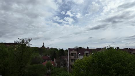Cloudy-sky-over-a-medium-sized-city,-spring-green-trees-in-the-background