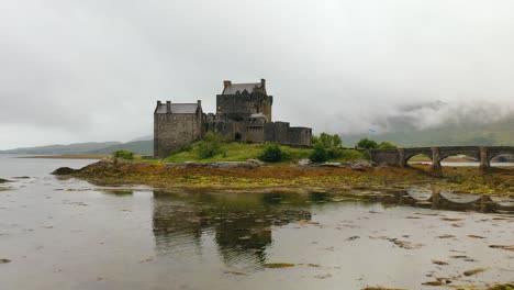 Impresionante-Toma-Aérea-Del-Castillo-De-Eilean-Donan-Reflejándose-En-El-Lago-Duich-En-Las-Tierras-Altas-De-Escocia.