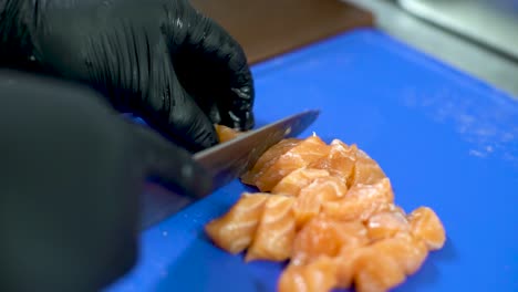 Chef-hands-with-black-gloves-cuts-salmon-cubes-on-a-cutting-board